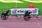 Dwie zawodniczki na sportowych wózkach inwalidzkich w trakcie biegu.