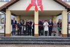 Grupa osób stoi przed budynkiem szkoły i przecina nożyczkami biało-czerwoną wstążkę