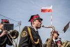 Strażak gra na saksofonie. Z tyłu widać flagę Polski na maszcie.
