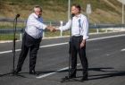Prezydent RP Andrzej Duda i minister Andrzej Adamczyk stoją na drodze i podają sobie ręce.