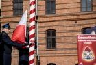 Strażacy wciągają biało-czerwoną flagę Polski na maszt.