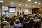 Sala konferencyjna. Na pierwszym planie siedzą ludzie na widowni.