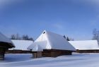 drewniane budynki w zimowej scenerii – brązowe drewniane ściany kontrastują z białymi, pokrytym śniegiem dachem i całym otoczeniem tonącym w puchu, nad całością błękitne, pogodne niebo