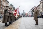 Żołnierze stoją szpalerem na placu. W tle widoczny pomnik.