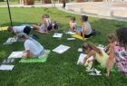 Dzieci siedzą na trawie i rysują.