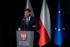 Wicemarszałek Łukasz Smółka w trakcie wystąpienia, w tle za nim widać flagi Unii, Polski i Małopolski. 