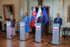 Zdjęcie przedstawia salę z flagami Polski i Słowacji. Po środku przy pulpitach konferencyjnych z godłem Słowacji stoją dwie kobiety, zaś przy pulpitach z godłem Polski dwaj mężczyźni. Osoby te reprezentują rządy obu państw. Obok stoi kobieta - tłumaczka.