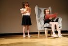 Dwie dziewczynki w trakcie występu na scenie, jedna z nich siedzi w fotelu