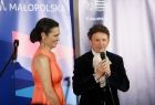Olga Bończyk (aktorka) i Jacek Wójcicki (aktor, śpiewak) podczas wspólnego występu. Jacek Wójcicki stoi i śpiewa do mikrofonu, Olga Bończyk stoi obok uśmiechnięta.