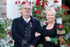 Iwona Gibas z zarządu województwa stoi uśmiechnięta wraz z dyrektorem muzeum. W tle widoczny krzak czerwonych róż.