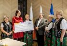 Członek zarządu Marta Malec-Lech wręcza promesę na 10 000 złotych grupie kobiet w strojach regionalnych i mężczyźnie w szarym garniturze.