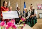 Członek zarządu Marta Malec-Lech trzymająca promesę. Za nią kobiety w strojach regionalnych i mężczyzna w szarym garniturze.