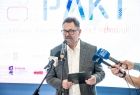 Krzysztof Głomb prezes Stowarzyszenia „Miasta w Internecie” mówi do mikrofonu. W tle widoczny napis: PAKT.