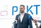 Janusz Cieszyński wiceminister ds. cyfryzacji mówi do mikrofonu. W tle widoczny napis: PAKT.