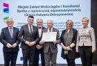 Beneficjenci z Kalwarii Zebrzydowskiej stoją na scenie z wicemarszałkami Łukaszem Smółką i Józefem Gawronem oraz Iwona Gibas z zarządu województwa.