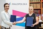 Członek zarządu Marta Malec-Lech i dyrektor stowarzyszenia w geście uścisku dłoni. W tle napis Małopolska.