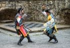 Dwóch walczących rycerzy w strojach historycznych na dziedzińcu zamku. 