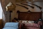 Widok na wnętrze zabytkowego pokoju zamkowego. Na który widać stare drewniane łóżko oraz muszkiety zawieszone na ścianie 