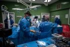 Pięć osób na sali operacyjnej w niebieskich fartuchach, czepkach, rękawiczkach i maseczkach ochronnych.
