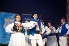 Zespół regionalny w tradycyjnych strojach ;ludowych występuję na scenie. Zespół tańczy parami. 