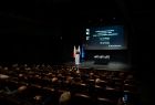 Widok na publiczność i stojącego przy szarej mównicy wicemarszałka Józefa Gawrona. W tle za nim wyświetlane są slajdy.