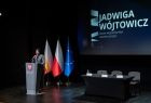 Radna Jadwiga Wójtowicz przemawia ze sceny. W tle za nią widać trzy flagi, Polski Unii i Małopolski. 