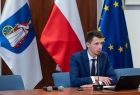 Przedstawiciel Urzędu Marszałkowskiego siedzący za stołem prezydialnym na tle flag