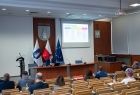 widok na salę w której odbywało się Forum na pierwszym planie uczestnicy Forum siedzący na widowni w tle stół prezydialny siedzący przy nim moderatorzy dyskusji, na ekranie jedna z prezentacji