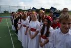 Grupa dziewczynek w białych sukienkach stoi na boisku szkolnym