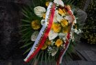 Kwiaty przed pomnikiem, przewiązane wstęgą z napisem "Zarząd Województwa Małopolskiego"