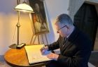  marszałek podczas wpisu do księgi kondolencyjnej; siedzi przy stoliku, na którym leży duża księga, obok pióro, lampka stojąca i obraz papieża