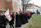 Przemarsz uczestników uroczystości. Na czele młode osoby w strojach historycznych oraz młodzi mężczyźni ze sztandarem z wyhaftowanym napisem W imię Boże