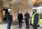 Widok na wnętrze remontowanych lub budowanych pomieszczeń, marszałek stoi wewnątrz pomieszczenia, którego ściany są w surowym stanie. Marszałkowi towarzyszy 3 mężczyzn. 