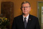Marszałek Witold Kozłowski. W tle widać pomieszczenie domu, po lewej stronie na stole leżą kwiaty