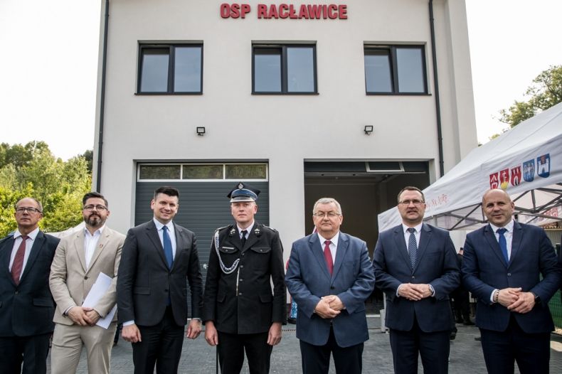 Wicemarszałek Łukasz Smółka stoi przed remizą z napisem OSP Racławice z innymi uczestnikami wydarzenia.