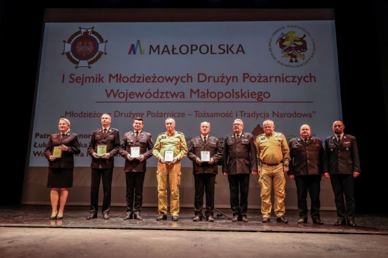 Wicemarszałek Łukasz Smółka stoi na scenie z innymi uczestnikami wydarzenia.