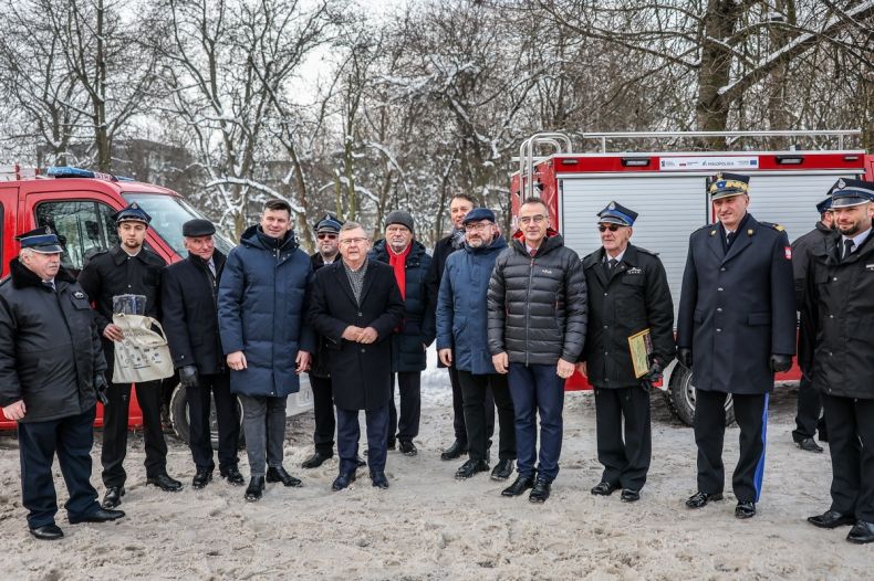 Marszałek Witold Kozłowski stoi ze strażakami przy wozach strażackich.