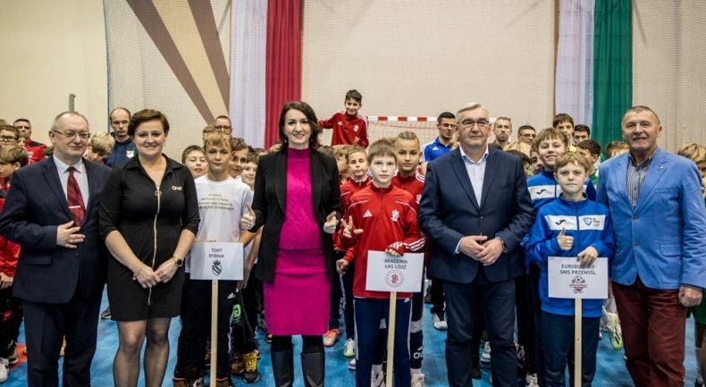 Marta Malec-Lech z zarządu województwa stoi z uczestnikami wydarzenia w hali sportowej.