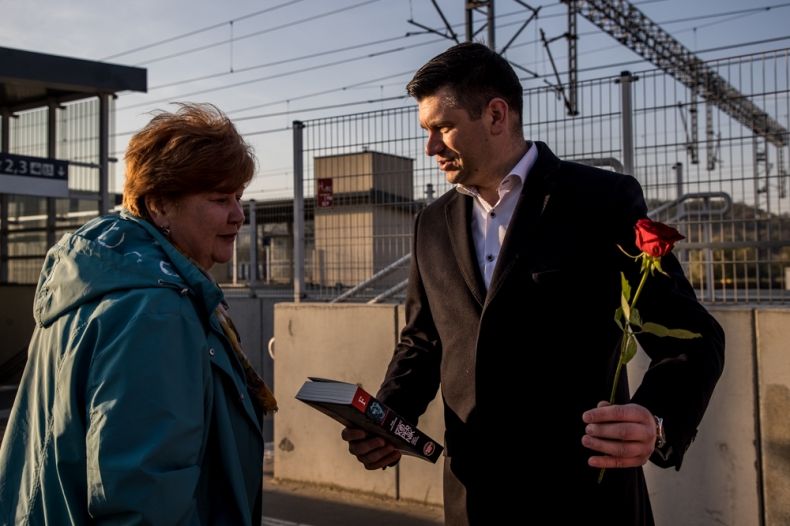 Wicemarszałek Łukasz Smółka trzyma w rękach książkę i różę. Obok stoi kobieta.