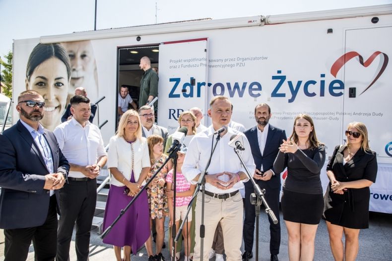 Wicemarszałek Łukasz Smółka stoi z prezydentem Andrzejem Dudą i innymi uczestnikami wydarzenia przed mammobusem.