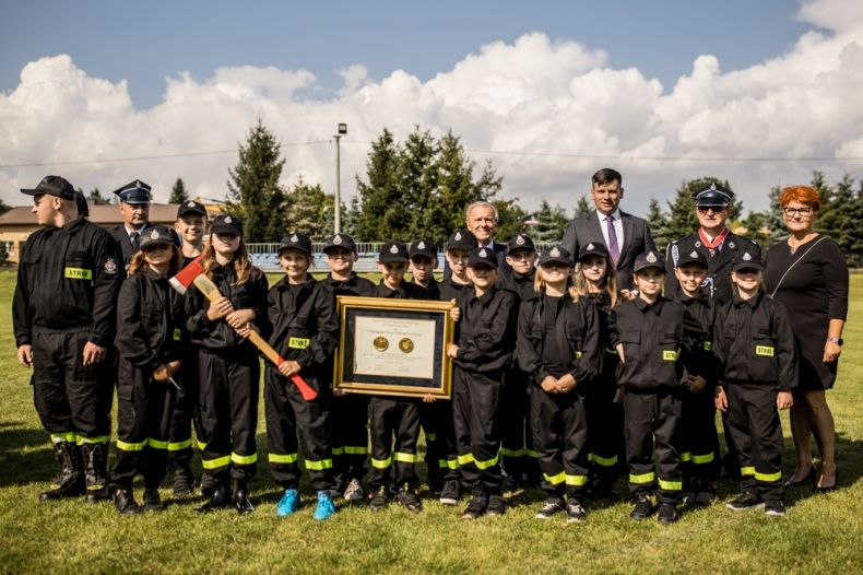 Wicemarszałek Łukasz Smółka stoi ze strażakami trzymającymi medal Polonia Minor.