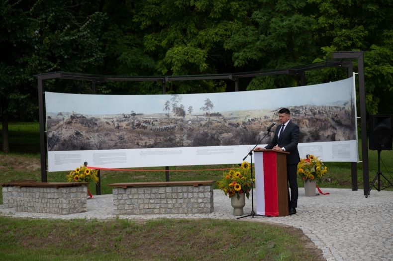 Wicemarszałek Łukasz Smółka stoi przed panoramą i przemawia.
