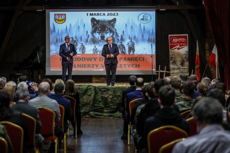 Wicemarszałek Józef Gawron stoi na scenie i mówi do mikrofonu. Obok stoi mężczyzna prowadzący wydarzenie.