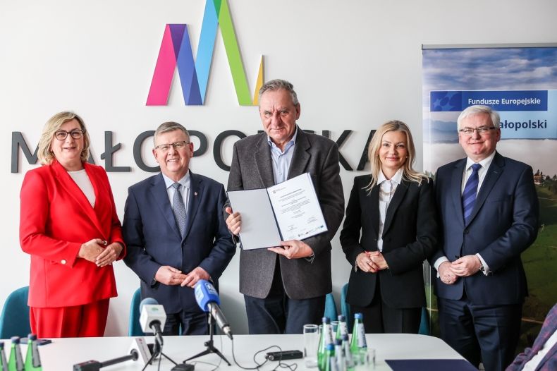 Mężczyzna w garniturze prezentuje podpisaną umowę. Obok marszałkowie i panie poseł.