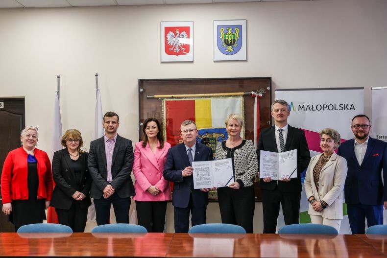 Wspólne zdjęcie uczestników wydarzenia w Brzeszczach. W centrum kadru: marszałek Witold Kozłowski, Iwona Gibas z zarządu województwa oraz burmistrz Radosław Szot prezentują podpisaną umowę 