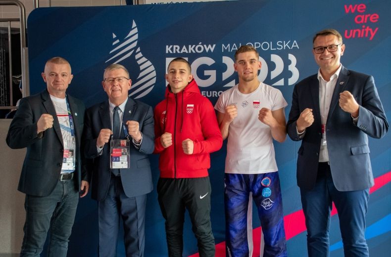 zdjęcie grupowe: marszałek, burmistrz i zawodnicy kickboxingu, na granatowej ściance z logotypem igrzysk