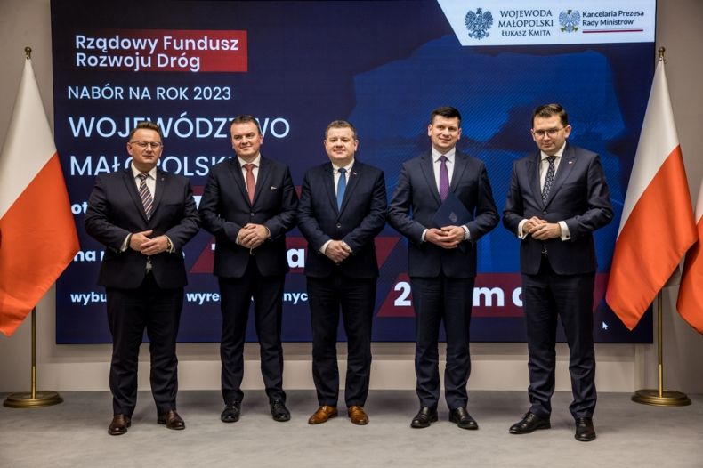 Wicemarszałek Łukasz Smółka stoi razem z wojewodą Łukaszem Kmita i innymi mężczyznami na scenie.