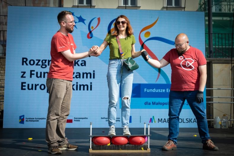 Ludzie stoją na scenie. Z tyłu napis Rozgrzewka z Funduszami Europejskimi.