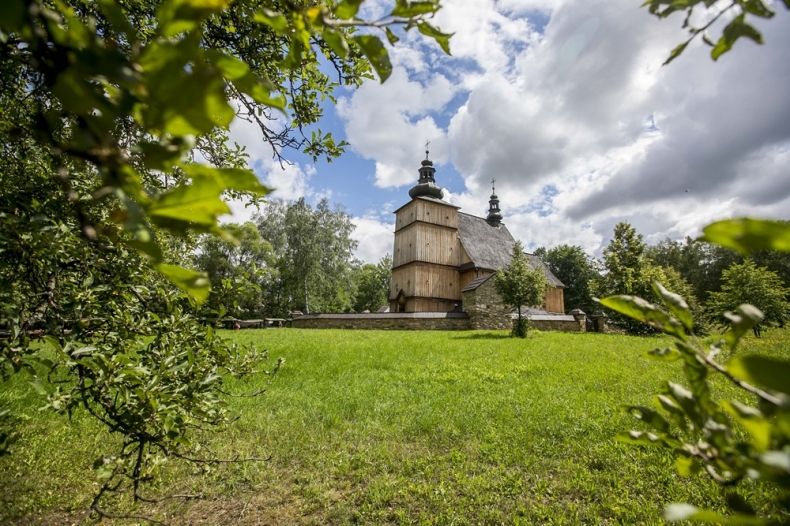 Krajobraz z zielenią, w tle widoczny drewniany kościół w skansenie 