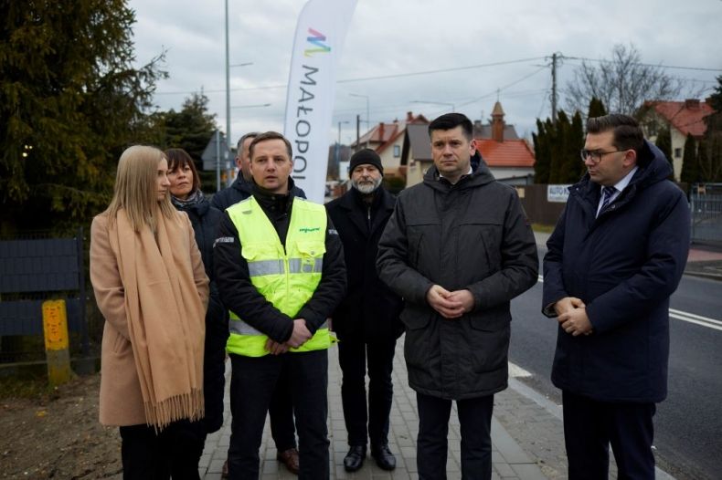 Wicemarszałek Łukasz Smółka stoi z uczestnikami wydarzenia przy drodze.